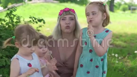 年轻的金发嬉皮士妈妈在公园里和她的小女孩一起吹蒲公英女儿们穿着类似的衣服视频的预览图