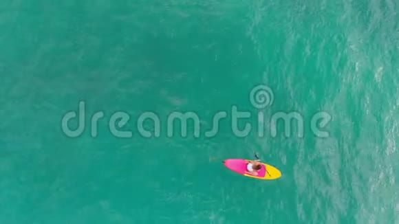 在蓝色海洋中站立桨板上的女人的空中视野视频的预览图