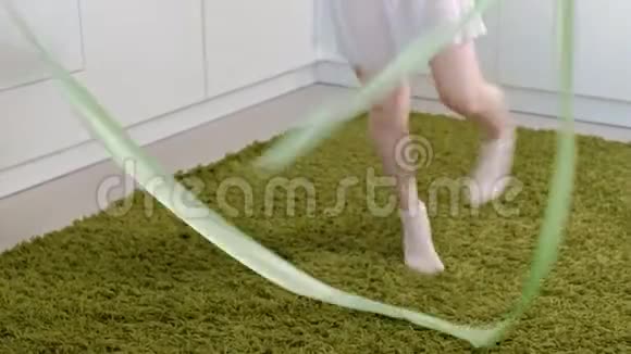 一个快乐的小女孩穿着白色体操泳衣训练用丝带跳舞进行艺术体操跳跃和视频的预览图