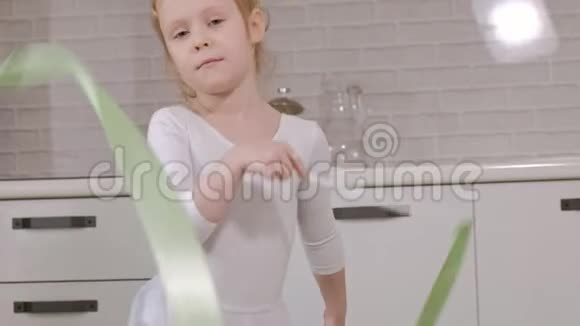 一个快乐的小女孩穿着白色体操泳衣训练用丝带跳舞进行艺术体操跳跃和视频的预览图