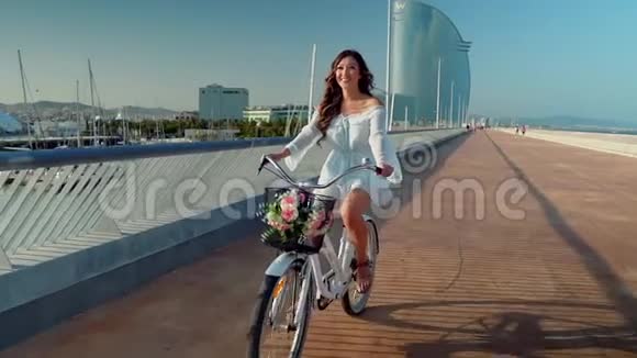 穿着蓝色连衣裙的亚洲模特骑着白色自行车在海上露台上视频的预览图