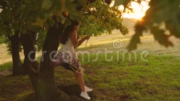 在森林里的一个夏天的晚上少女喜欢在秋千上飞行年轻女孩在橡树上的绳索秋千上摇摆视频的预览图