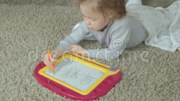 一个红色波浪发的小女孩躺在地板上画在一块磁板上教育过程的概念视频的预览图