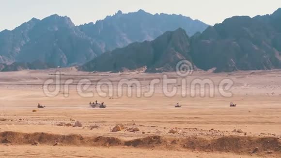 在埃及的沙漠中骑四方自行车小组以山脉为背景驾驶ATV视频的预览图