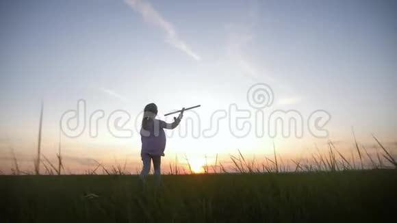 可爱的女孩在日落时在田里玩玩具木飞机儿童在木飞机上玩的剪影视频的预览图