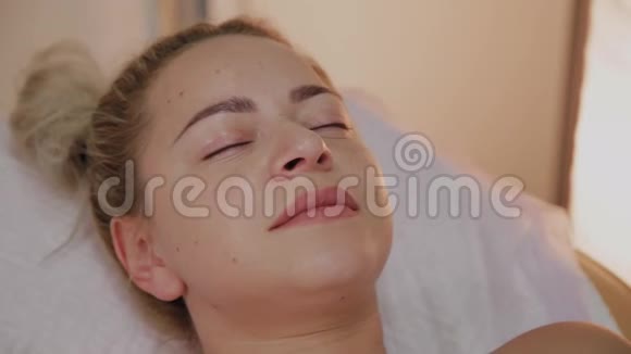 美丽的年轻女性穿着浴袍躺在豪华水疗沙龙等待面部护理程序视频的预览图