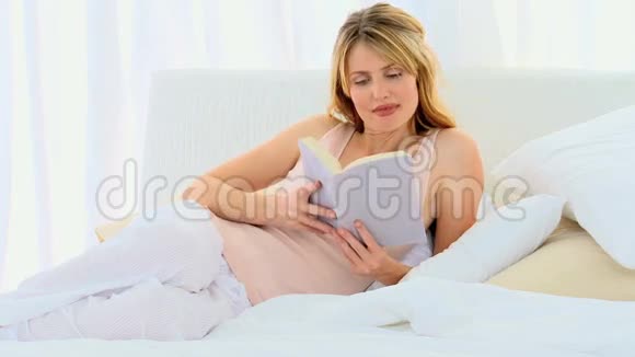 可爱的金发女人在床上看书视频的预览图