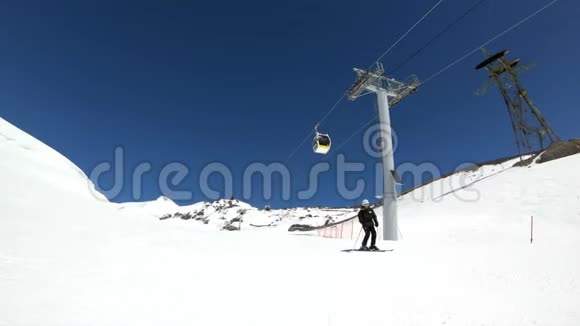 阳光明媚的一天一个身穿黑色装备戴着滑雪杆的白色头盔的宽角男滑雪者骑在雪坡上视频的预览图