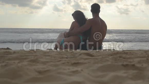 年轻的浪漫夫妇正坐在海滩上拥抱着美丽的景色一个女人和一个男人坐在一起视频的预览图