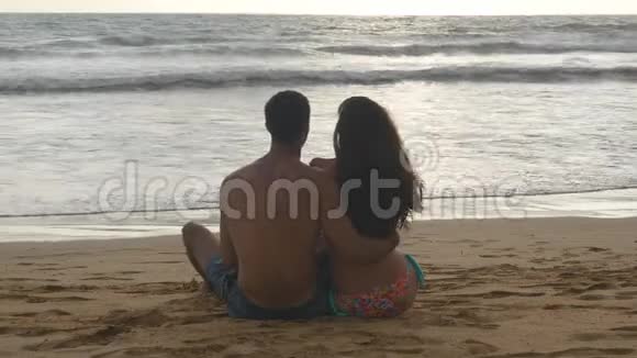 年轻的浪漫夫妇正坐在海滩上拥抱着美丽的景色一个女人和一个男人坐在一起视频的预览图