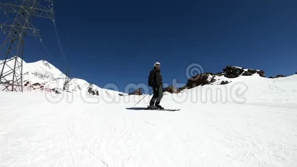 阳光明媚的一天一个身穿黑色装备戴着滑雪杆的白色头盔的宽角男滑雪者骑在雪坡上视频的预览图