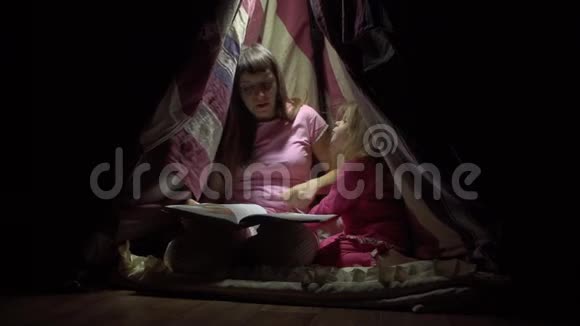 妈妈和孩子女儿晚上在帐篷里看一本带手电筒的书视频的预览图