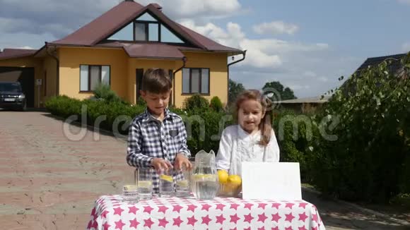 两个小孩在阳光明媚的日子里在自制的柠檬水摊上卖柠檬水上面写着一个企业家的价格标志视频的预览图