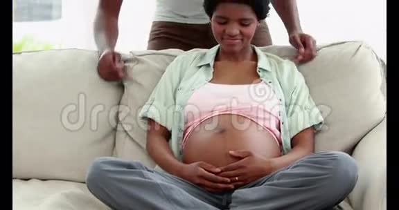 抱着丈夫坐在沙发上微笑的孕妇视频的预览图