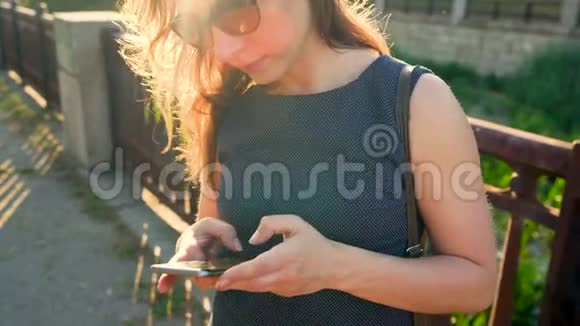 日落时分戴太阳镜的女人在户外使用智能手机视频的预览图