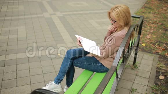 金碧辉煌的女子读书书在秋天的公园里视频的预览图