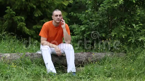 一个拿着手机的人坐在森林里一棵倒下的树上视频的预览图
