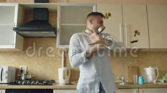 有魅力的年轻风趣男子在家厨房做饭时用瓢泼大雨跳舞唱歌视频的预览图