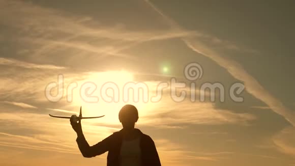 孩子们在太阳的背景下手里拿着一架飞机女孩在日落时玩玩具飞机飞行的梦想快乐视频的预览图