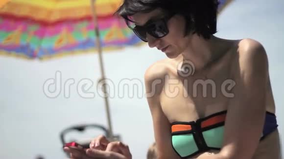 在海滩上使用智能手机的年轻女人视频的预览图