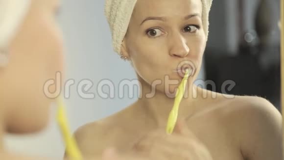 镜子里的一个美丽的女人头上有毛巾在浴室里刷牙视频的预览图