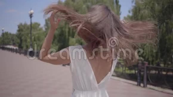 可爱的年轻女孩戴着太阳镜和一件白色的夏季时装长裙走在户外一个漂亮女人的闲情逸致视频的预览图