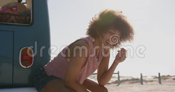 在海滩上坐着露营车的年轻女子视频的预览图