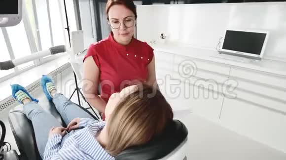 一个年轻的女孩在与一个戴眼镜的牙医女士协商时正坐在一张椅子上的一个雄蕊学办公室这就是视频的预览图