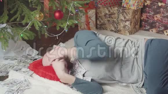 一个男人正在和很多钱和一棵圣诞树上床视频的预览图