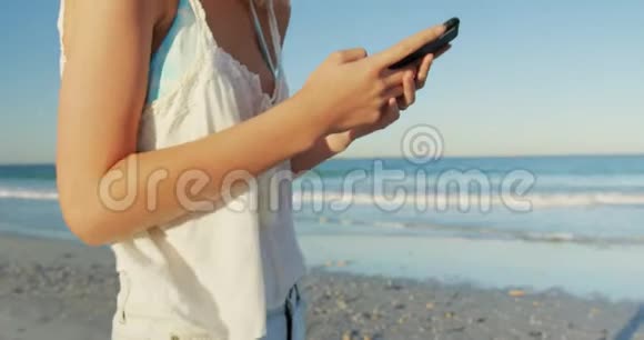 在海滩上使用智能手机的年轻女性视频的预览图