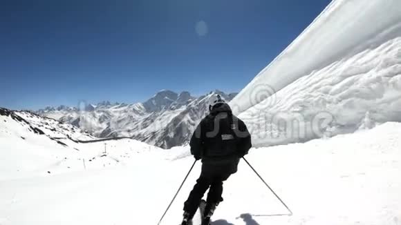 阳光明媚的一天一个身穿黑色装备戴着滑雪杆的白色头盔的宽角男滑雪者骑在雪坡上视频的预览图