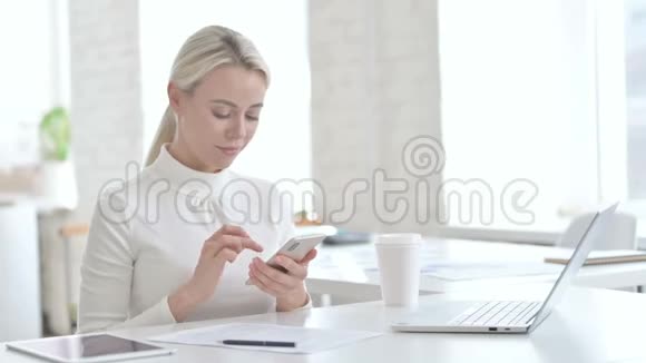 年轻的女商人在办公室里使用智能手机视频的预览图