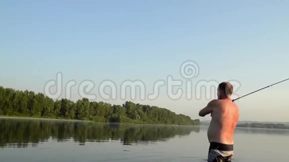 渔夫在一条平静的河里钓鱼一个穿着渔具的人在河里站着扔一根鱼竿视频的预览图