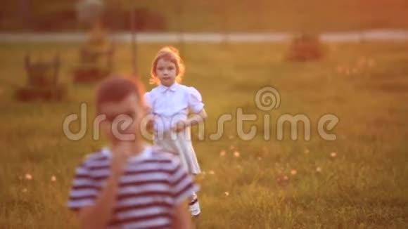 小男孩和小女孩跑着玩他们吹蒲公英日落视频的预览图