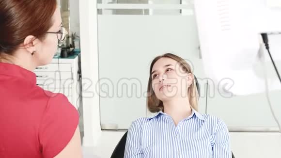 一个年轻的女孩在与一个戴眼镜的牙医女士协商时正坐在一张椅子上的一个雄蕊学办公室这就是视频的预览图