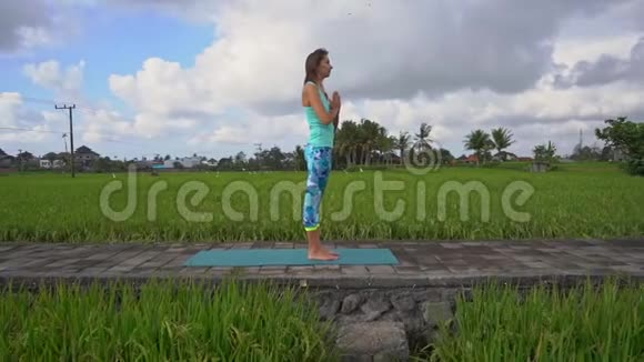 一个年轻女子用瑜伽数学在美丽的稻田里行走时的慢动作稳定镜头视频的预览图