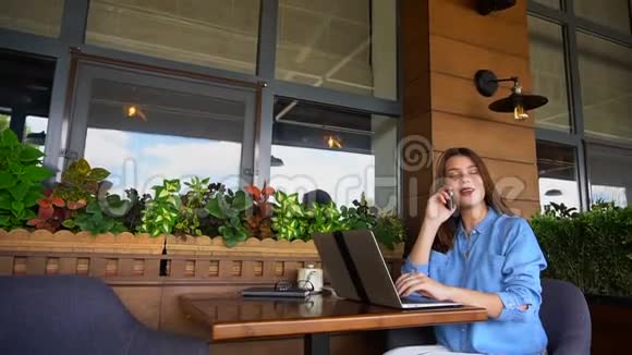 自由职业者通过智能手机交谈并与笔记本电脑在咖啡馆工作视频的预览图