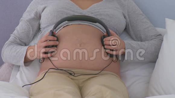 怀孕的女人在家里给肚子戴上耳机视频的预览图