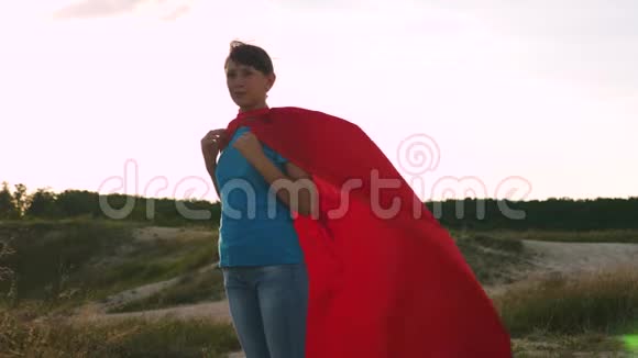 超级英雄女孩穿着红色斗篷站在战场上斗篷在风中飘扬慢动作美丽的女孩梦想视频的预览图