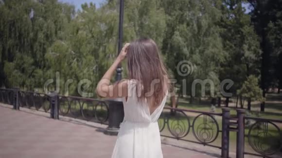 可爱的年轻女孩戴着太阳镜和一件白色的长夏时装走在户外一个漂亮女人的闲情逸致视频的预览图