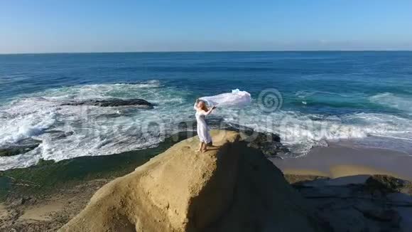 自由概念穿着白色连衣裙和围巾的女人站在岩石上跳舞在飞行视频的预览图