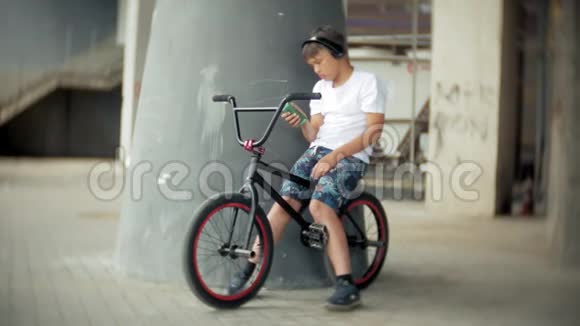 男孩坐在BMX自行车上听智能手机上的音乐视频的预览图