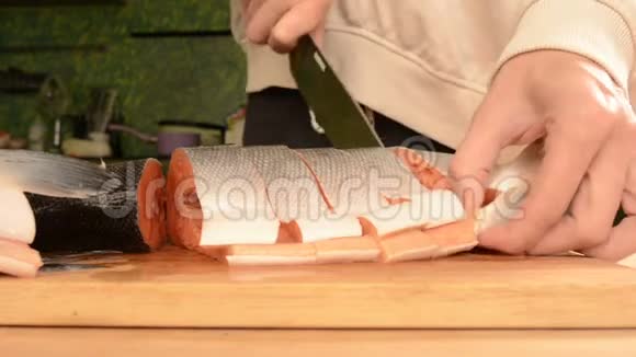 女性手的特写用刀子切一大条鲑鱼放在木制的家庭烹饪桌上视频的预览图