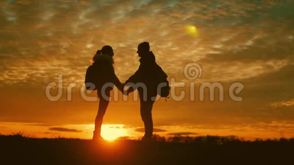 两个徒步旅行者的剪影带背包从山顶欣赏日落景色享受日落美景视频的预览图