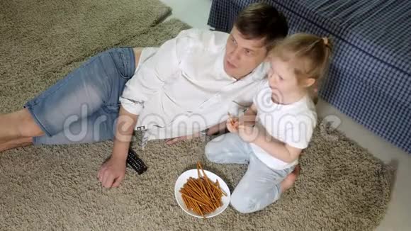 男人和女儿看电视坐在地上吃零食视频的预览图