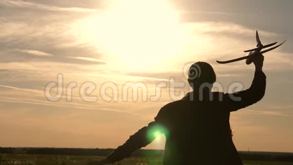 孩子们在太阳的背景下手里拿着一架飞机女孩在日落时玩玩具飞机飞行的梦想快乐视频的预览图