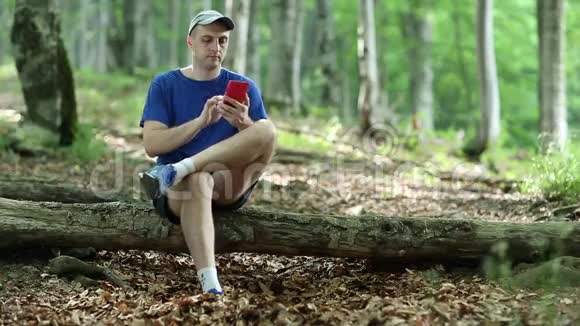 一个带着手机的人坐在森林里倒下的树上视频的预览图