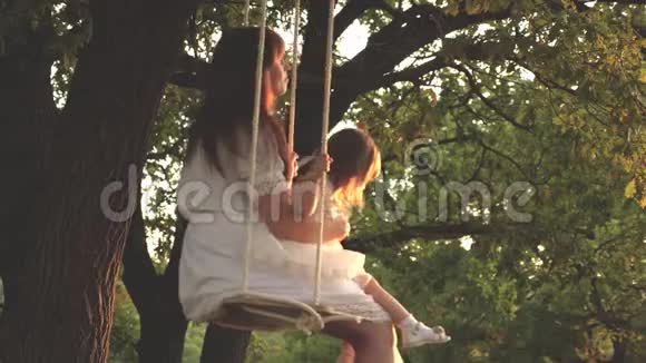 母亲和婴儿在森林里的橡树枝上用绳子摆动女孩笑高兴公园里的家庭乐趣大自然中的视频的预览图