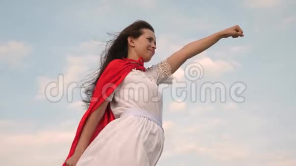 美丽的超级英雄女孩站在一片红色斗篷的田野上斗篷在风中飘扬女孩梦想成为一个视频的预览图