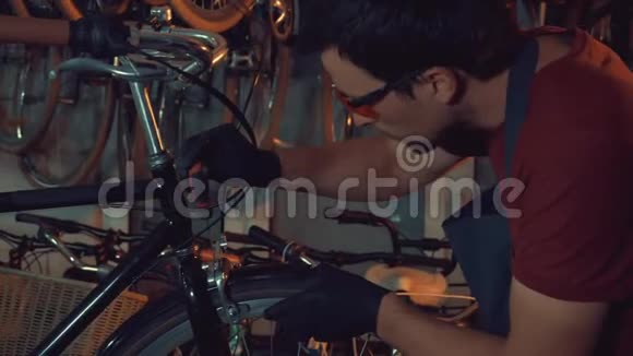 主题小企业自行车修复年轻的白种人黑发男子戴着安全眼镜手套和围裙使用手工工具修理视频的预览图
